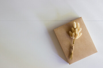 A craft gift box and flowers over the white wooden background with nature light. 