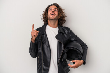 Young biker caucasian man holding a motorbike helmet isolated on gray background pointing upside...