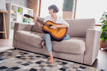 Full length body size photo young woman playing guiter sitting on coach alone in apartment