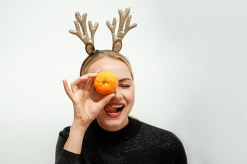Beautiful Santa girl with reindeer antlers. Happy blonde in a black sweater has closed her tangerine eye and shows her tongue