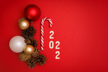 Christmas mockup with New Years balls, pine cones, candy cane and 2022 numbers on a red background with place for text. View from above. Horizontal format. Copyspace