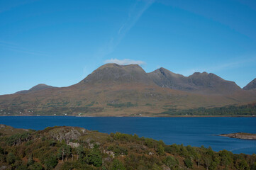 View over forest and Loch Torridon to Beinn Alligin mountain in the Scottish Highlands. Sunny day with blue. Clear view of ridgeline and horns of Alligin. No people.