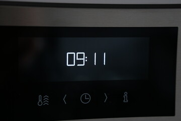 modern digital clock on oven is showing the time 09:11 in white digital numbers on black surface