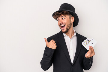 Young arab wizard man holding a magic cards isolated on white background points with thumb finger...