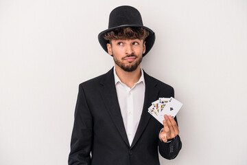Young arab wizard man holding a magic cards isolated on white background confused, feels doubtful...
