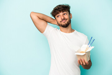 Young arab man holding a take away noodles isolated on blue background touching back of head, thinking and making a choice.