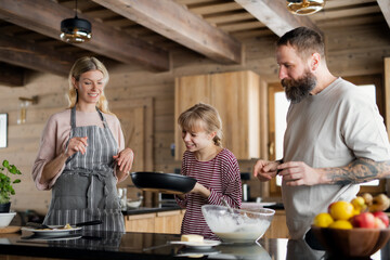 Family with small daughter cooking indoors, winter holiday in private apartment.