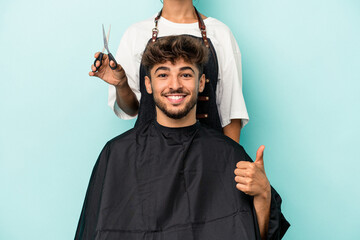 Young arab man ready to get a haircut isolated on blue background smiling and raising thumb up
