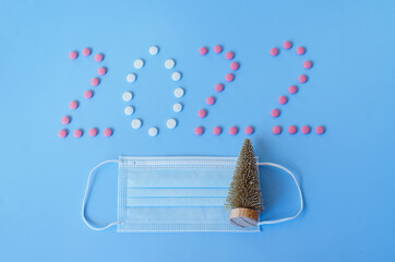 Christmas, New Year flat lay on blue background. numbers 2022 making with pills and medical mask. Top view. Copy space. Mock up. Concept of health care. New normal life after COVID-19. Copy space.