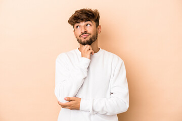 Young arab man isolated on beige background thinking and looking up, being reflective, contemplating, having a fantasy.