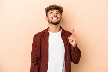 Young arab man isolated on beige background indicates with both fore fingers up showing a blank...