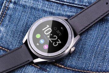 Smart watch in a matte metal case with a black leather strap next to the phone on a background of...