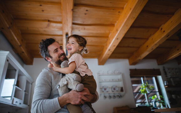 Low angle view of mature father with small daughter having fun indoors at home, holding and hugging.