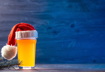 Glass of beer Christmas ale in Santa's red hat , blue wooden background for copy space