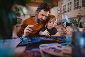 Mature father with two small children resting indoors at home, painting pictures.