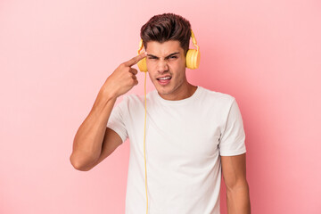 Young caucasian man listening to music isolated on pink background showing a disappointment gesture...