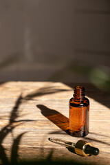 Dark amber glass bottle with dropper for oil, lotion or serum on a aged wooden background with a hard shadow of tropical palm leaves. Presentation of a cosmetic product. Layout of the beauty salon .