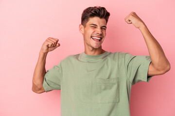 Young caucasian man isolated on pink background raising fist after a victory, winner concept.