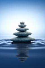 Fototapeta na wymiar Stack of stones with ripples in the water with blue reflections - zen and nature concept