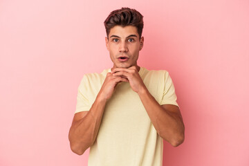 Obraz premium Young caucasian man isolated on pink background praying for luck, amazed and opening mouth looking to front.