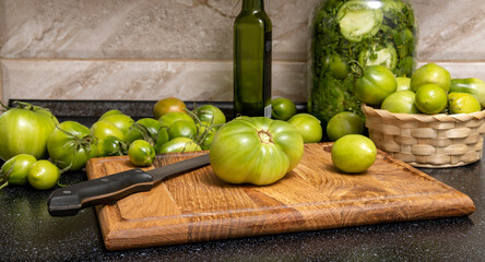 Fresh juicy green tomatoes,wooden board and basket full of it.Glass jar of green tomato preserves.Empty space