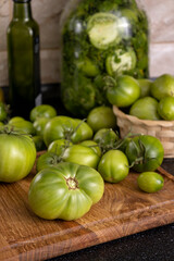 Vertical image.Fresh green tomatoes on the wooden cutting board and in basket,glass jar,bottle on the black kithcen table