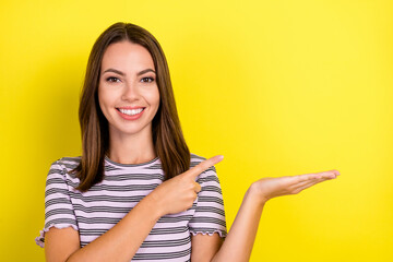 Photo of cute millennial brunette lady point hold empty space wear striped t-shirt isolated on yellow background