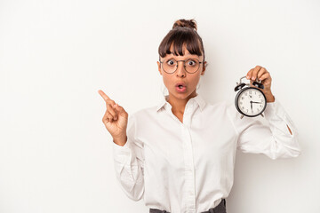 Young mixed race business woman holding an alarm clock isolated on white background  pointing to...