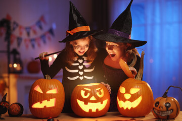 Happy family mother and little girl daughter in witch costumes celebrating Halloween at home