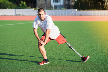 Young caucasian brunette male with prosthetic leg doing lunge at the stadium on the field. Sport...