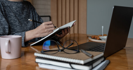 Close up female student using online learning on laptop, watching webinar and writing notes in notebook, doing study research