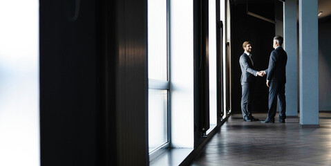 Full length view of businessmen shaking hands in office building.