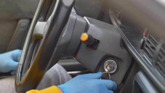 The driver wearing protective gloves turns the ignition key in the car and starts the car. close-up