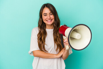 Young caucasian woman holding a megaphone isolated on blue background laughing and having fun.