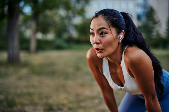 Asian woman taking a moment to catch her breath after workout in park