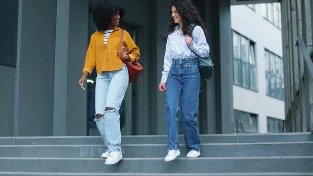 Two joyful and beautiful diverse young women walking the city together and having fun. Two girls going down stairs outdoor. Friendship concept