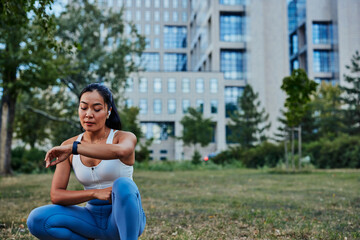 Fototapeta premium Young sportswoman looking and touching on smartwatch screen while exercise outdoors