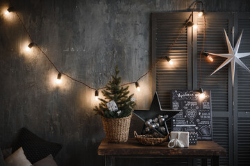 an element of the design of the New Year's interior in dark color in the loft style with a poster table, a small Christmas tree, light bulbs and decoration