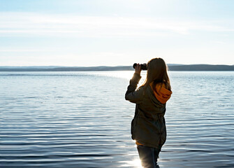 Young woman looking through binoculars at birds on lake Birdwatching, zoology, ecology. Research in...