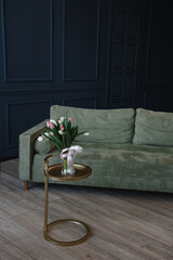 interior design of an apartment with dark blue walls, a green sofa and a golden small table with a vase and a bouquet of spring flowers