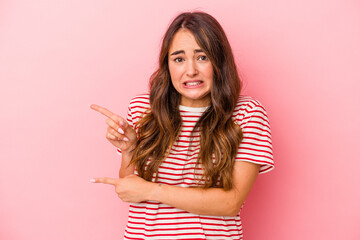 Young caucasian woman isolated on pink background shocked pointing with index fingers to a copy space. - obrazy, fototapety, plakaty