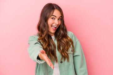 Fototapeta premium Young caucasian woman isolated on pink background stretching hand at camera in greeting gesture.