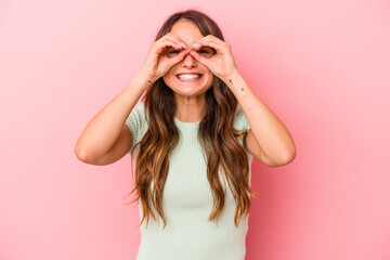 Young caucasian woman isolated on pink background showing okay sign over eyes