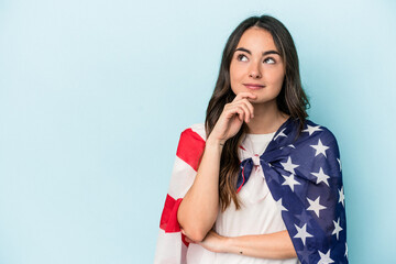 Young caucasian woman holding an American flag isolated on blue background looking sideways with...