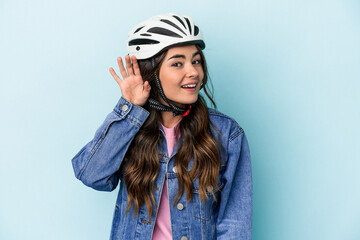 Young caucasian woman rinding a bike isolated on blue background trying to listening a gossip.
