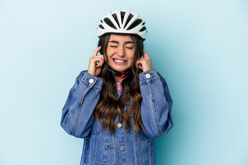 Young caucasian woman rinding a bike isolated on blue background covering ears with hands.