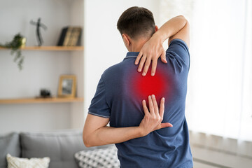 Pain between the shoulder blades, man suffering from backache at home