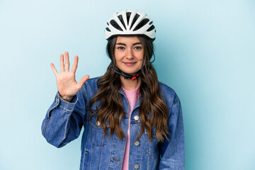 Young caucasian woman rinding a bike isolated on blue background smiling cheerful showing number...