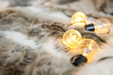 Garland lamps lie on a fluffy, cozy fur blanket. Coziness and atmospheric mood in the home...