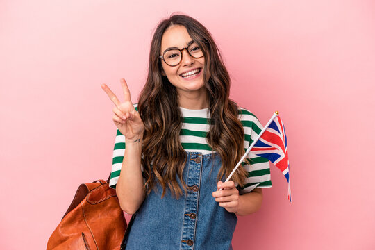 Young caucasian student woman studying English isolated on pink background joyful and carefree showing a peace symbol with fingers.